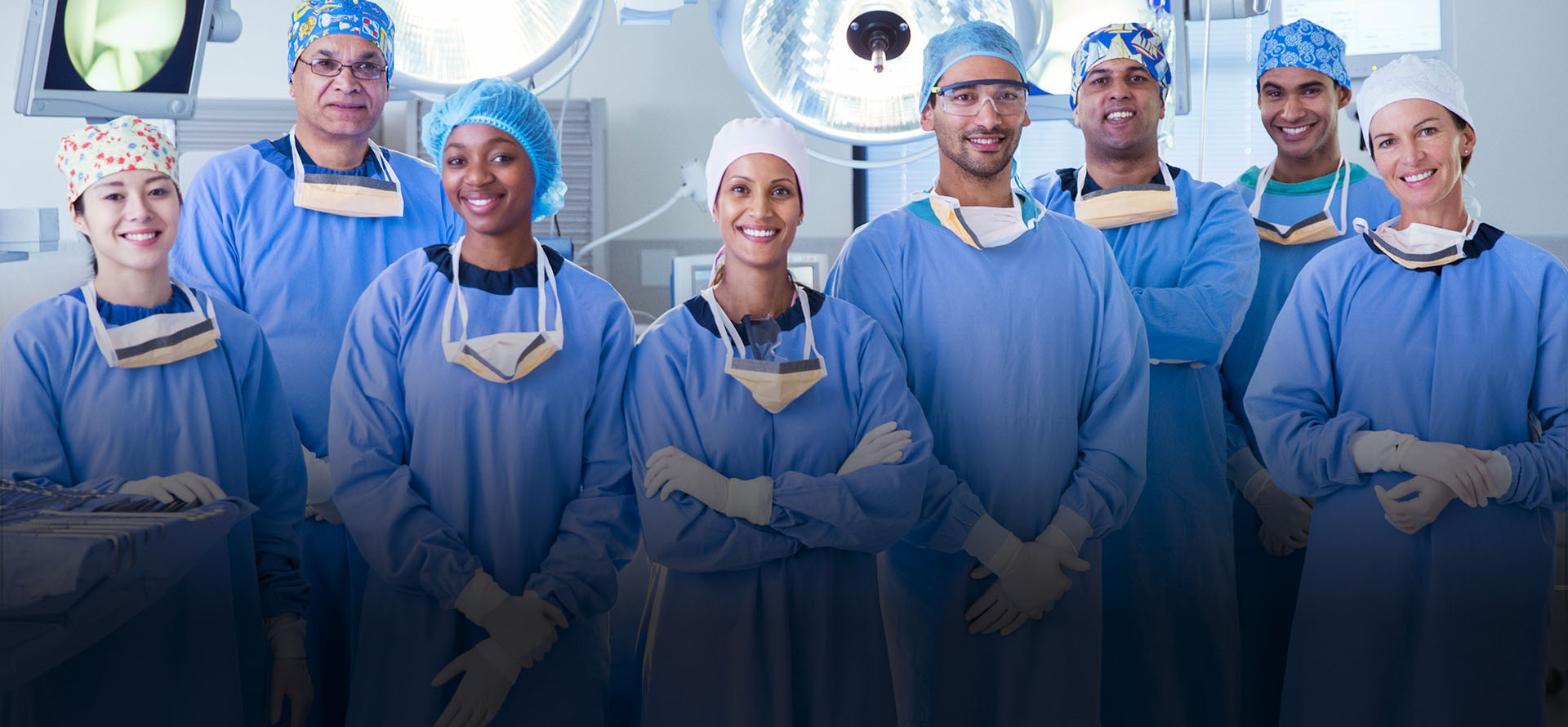 A group of smiling people in blue OR gear in an operating room