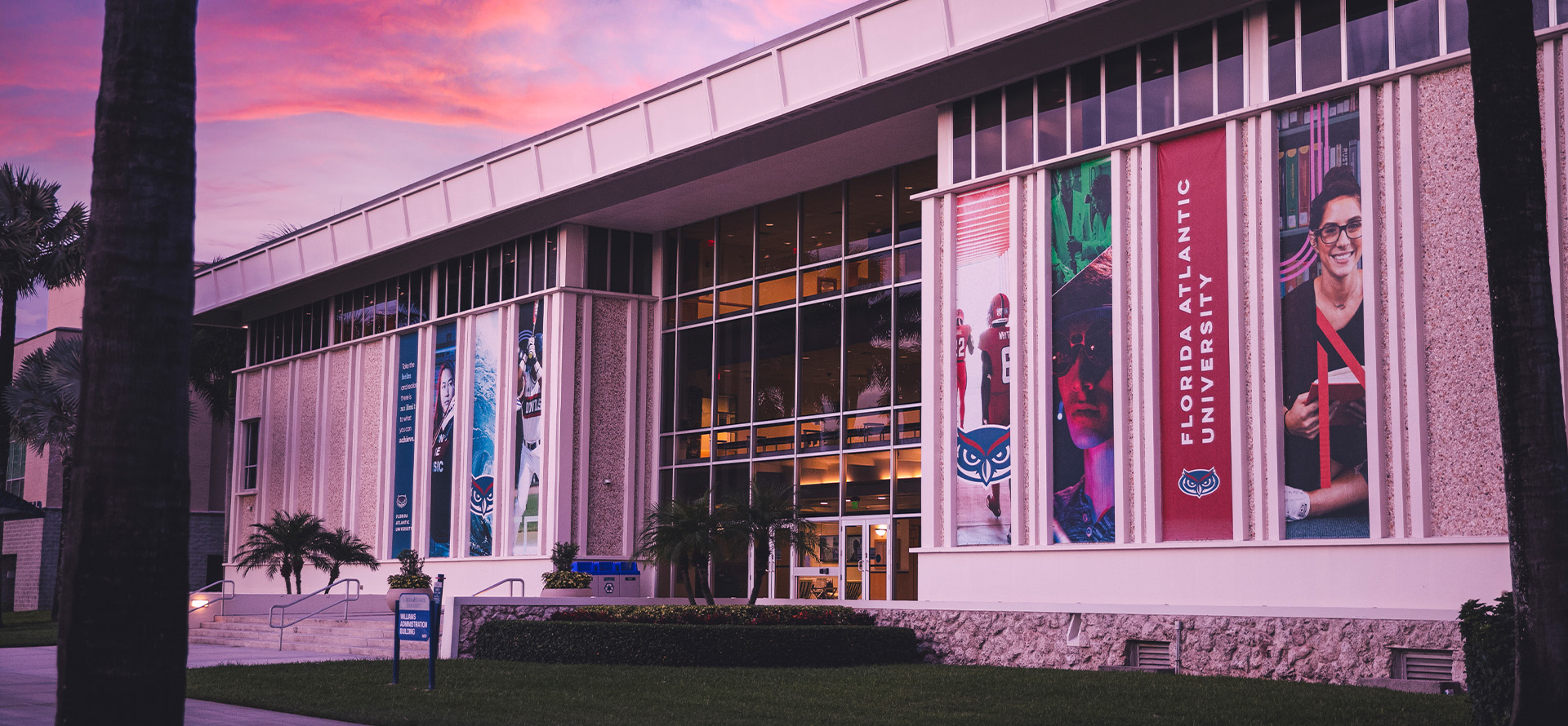 Contemporary building with glass windows and banners during sunset.