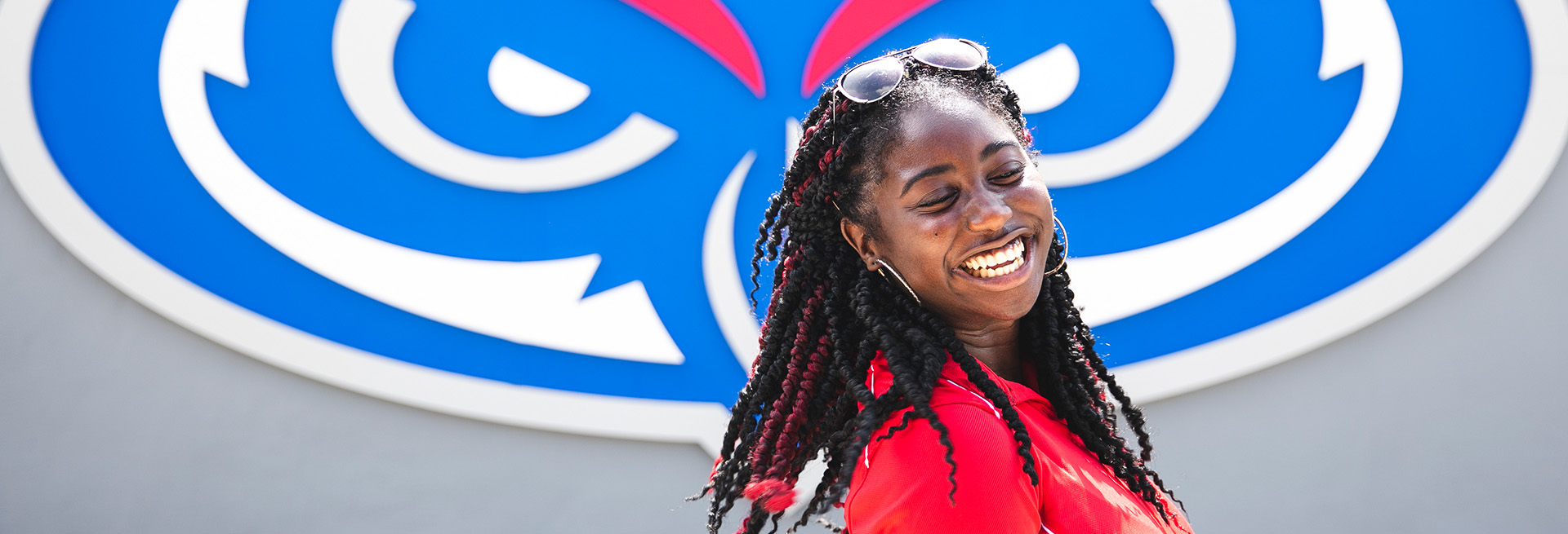 Student smiling infront of FAU Owl head logo sign