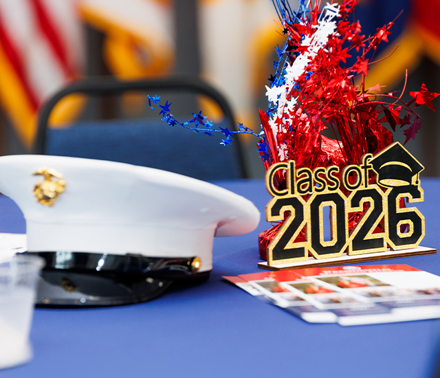 Military graduation decorations on a blue tablecloth with a Marine dress had and 2026 center piece