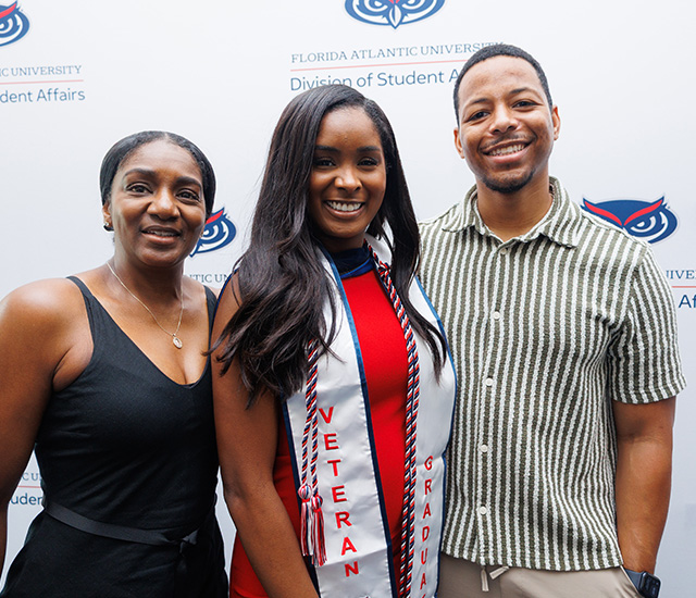 Student posing and parents with military graduation sash in front of a Military background