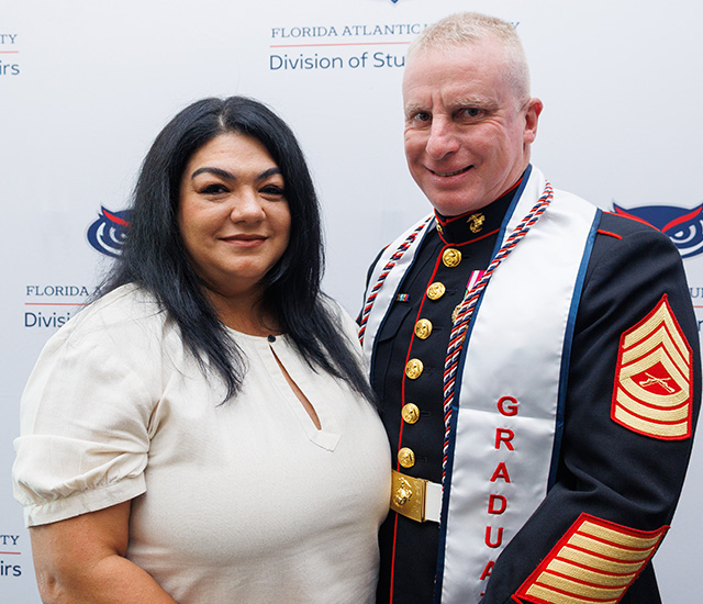 Student with significant other posing and military graduation sash in front of a Military background