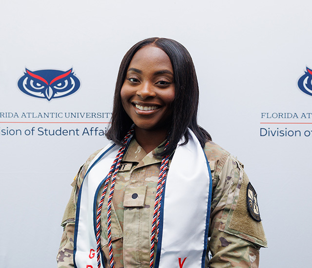 Student posing with military graduation sash in front of a Military background
