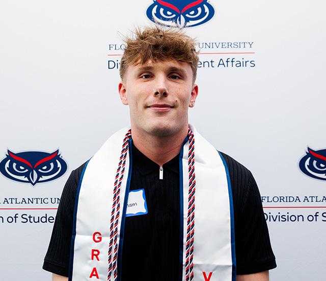 Student posing with military graduation sash in front of a Military background