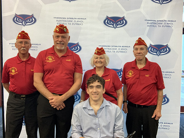 Service members pose in front of a step and repeat banner
