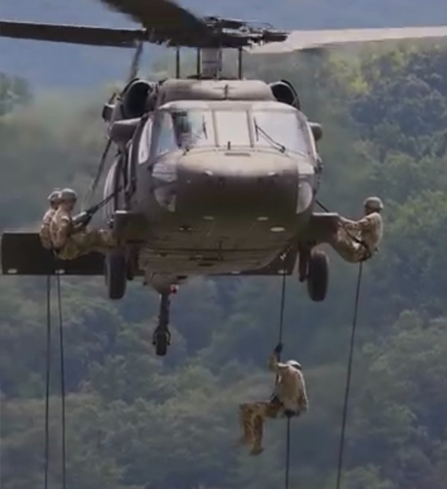 military helicopter hovering with troops scaling to the ground on ropes